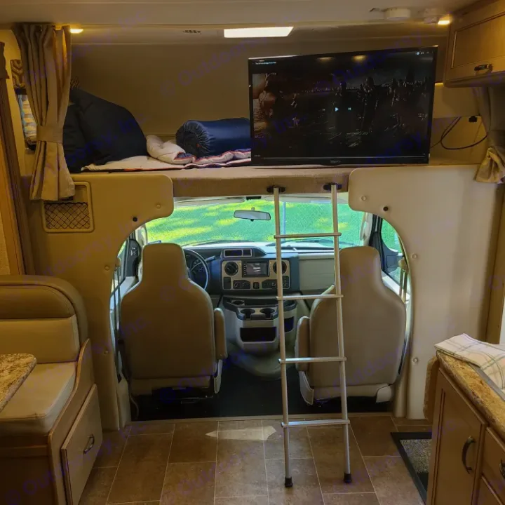 Cozy rv rental interior featuring an over-cab bed with TV, ladder, and a view into the front cab area.. Thor Motor Coach Chateau 2019