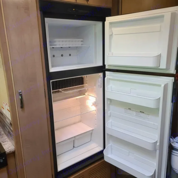 Inside an RV rental kitchen, a clean, empty two-door refrigerator/freezer, ready for your adventure.. Thor Motor Coach Chateau 2019