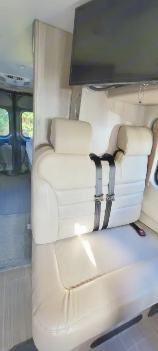 Step into this RV rental: a light-colored bench seat with two seatbelts, ideal for travel, under a mounted TV.. Thor Sequence 2021