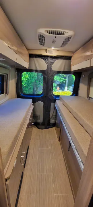 Interior of an RV rental with a narrow aisle between two beds, overhead cabinets, and a ceiling AC unit, ready for adventure.. Thor Sequence 2021