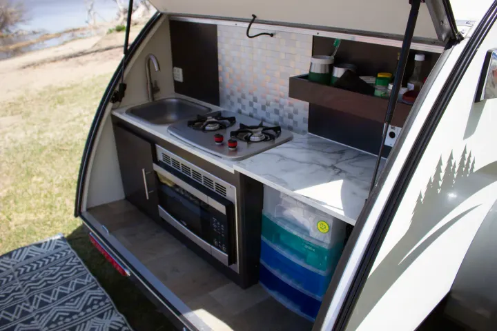 This RV rental's compact outdoor kitchen features a sink, two-burner stove, and microwave, perfect for camping adventures.. nuCamp T@G 2022