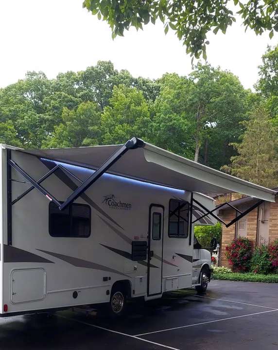 Coachmen Freelander RV rental with an extended, lit awning, parked outdoors among green trees.. Forest River Coachmen Freelander 2021