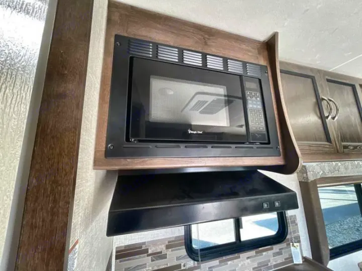 Explore this RV rental's kitchen: a black built-in microwave, range hood, and wood-grain cabinets for easy meals on the road.. Coachmen Freelander 27QB 2020