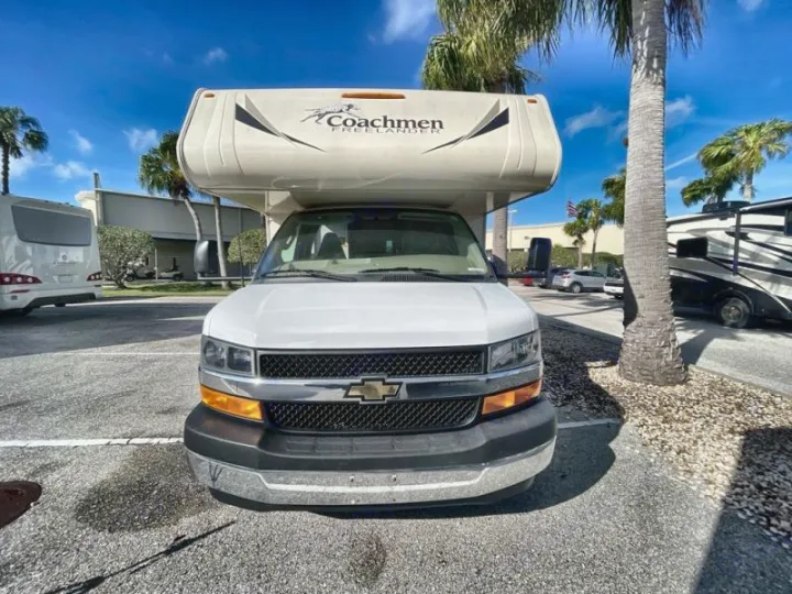 Front view of a white Coachmen Freelander RV rental on a sunny day, parked amidst palm trees and other motorhomes.. Coachmen Freelander 27QB 2020