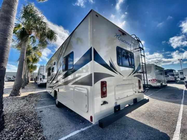 This cream Coachmen Freelander RV rental, with a rear ladder, is ready for adventure in a sunny lot bordered by palm trees.. Coachmen Freelander 27QB 2020