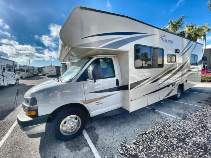 A white Coachmen Freelander Class C rv rental on a sunny lot, ready for your trip. Other RVs and palm trees visible.. Coachmen Freelander 27QB 2020