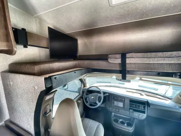 RV rental cockpit below a cab-over bunk with a mounted TV. Experience comfort & convenience on your road trip.. Coachmen Freelander 27QB 2020