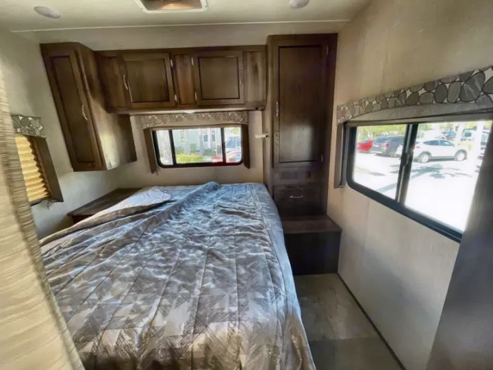 This RV rental bedroom features a large bed, wooden cabinets, and windows offering exterior views. Ideal for your next trip.. Coachmen Freelander 27QB 2020