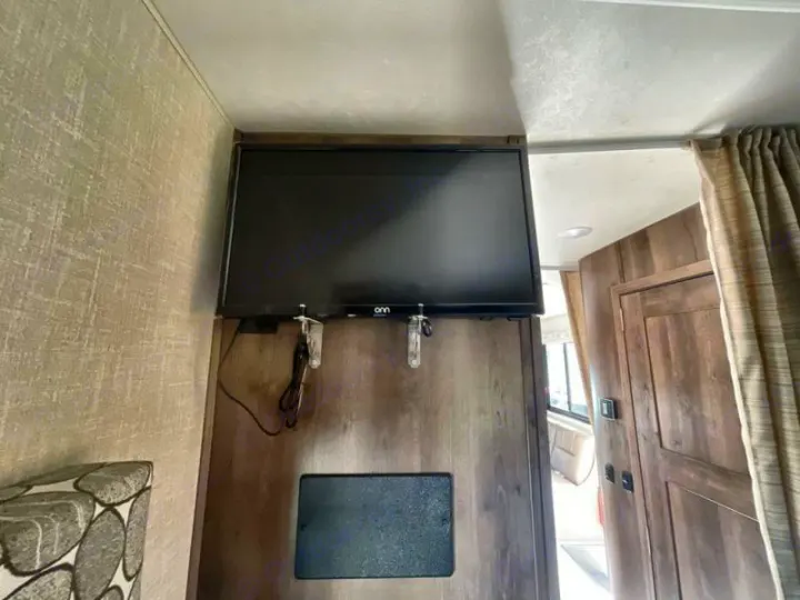 Relax in your rv rental with this mounted TV, perfect for entertainment. View of a modern RV interior with a wooden door.. Coachmen Freelander 27QB 2020