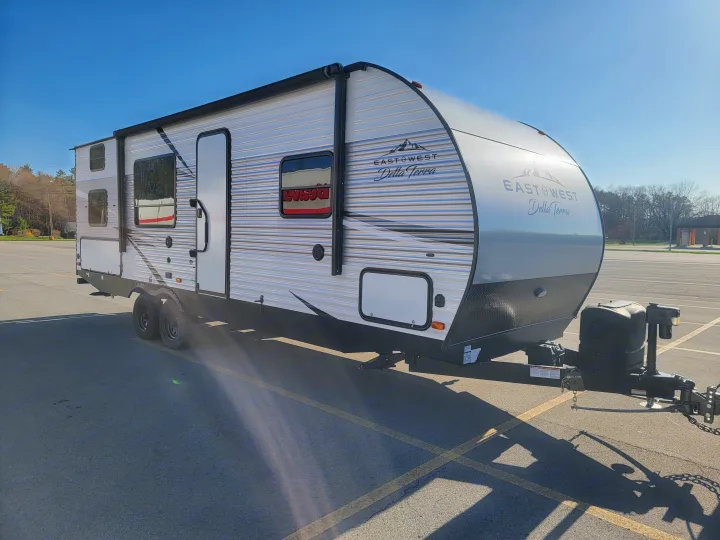 A white and grey East West Della Terra travel trailer sits on an asphalt lot. Explore this RV rental for your next camping trip.. East to West Della Terra 2021