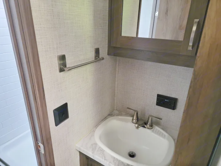This RV rental bathroom features a compact sink, marble-look counter, mirrored cabinet, and GFI outlet. Ideal for travel.. East to West Della Terra 2021