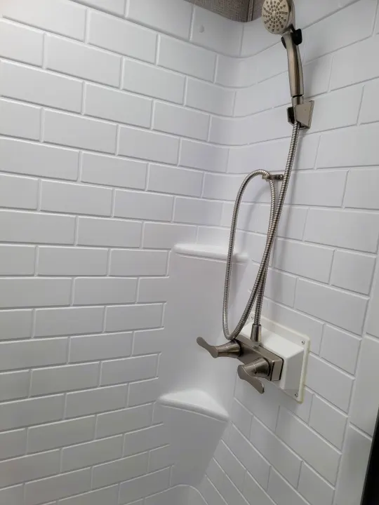 Compact shower in an RV rental, featuring a handheld sprayer and white subway tile-look walls.. East to West Della Terra 2021