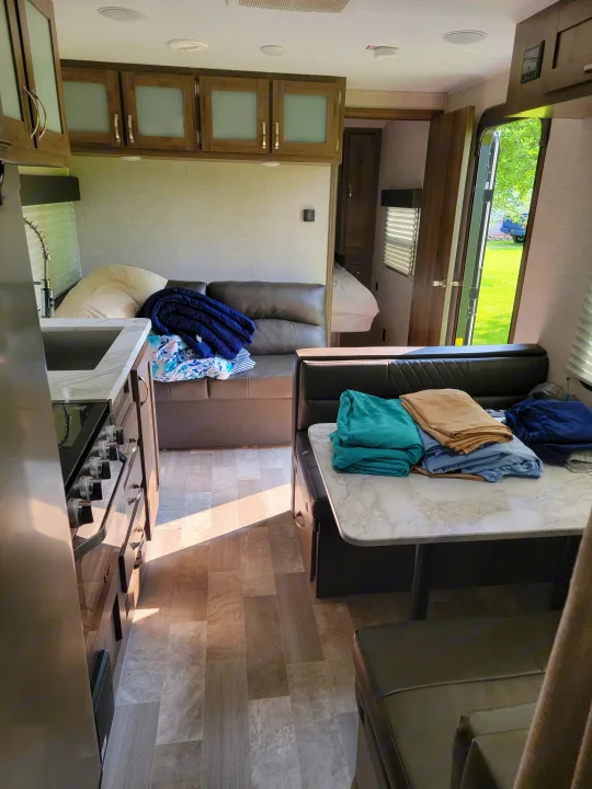 RV rental interior: modern dinette, kitchen with stove/sink, storage cabinets, and a large window view.. East to West Della Terra 2021