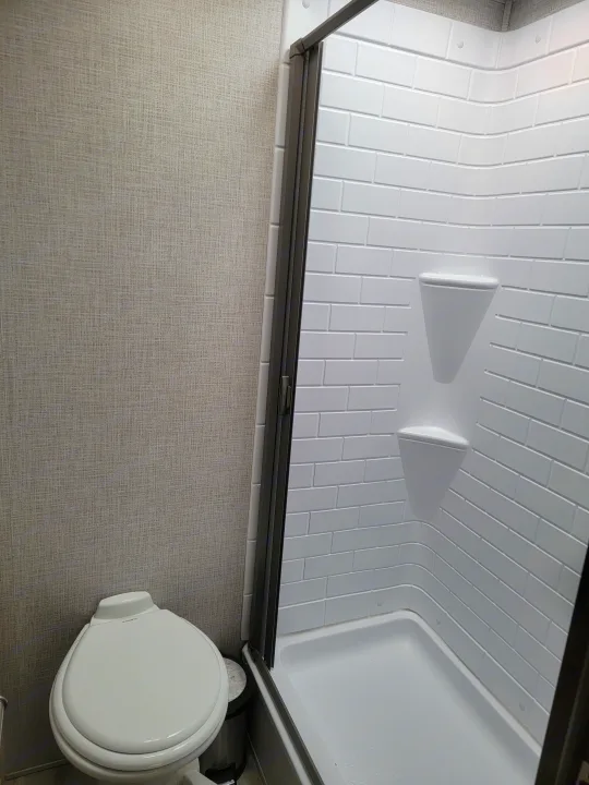 Experience comfort in this RV rental bathroom with a white, subway-tile textured shower and compact toilet.. East to West Della Terra 2021