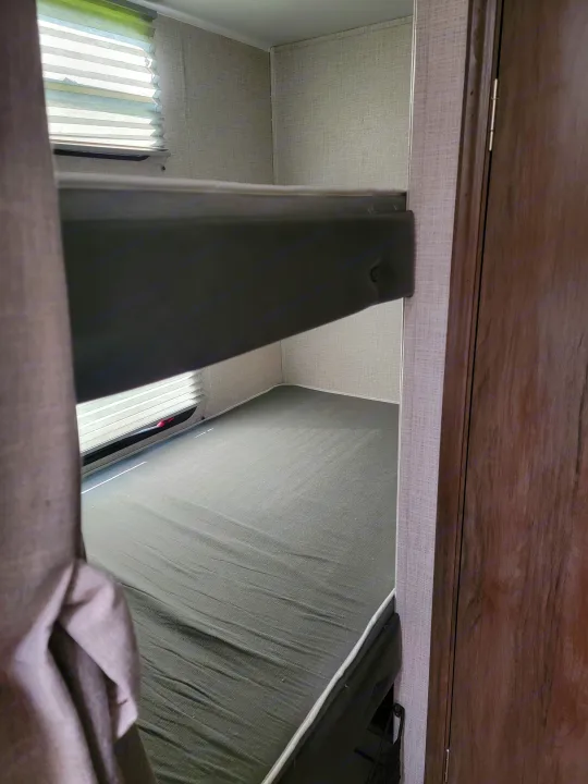 RV rental: View from below an RV bunk bed, showing the mattress, window with blinds, and cabinet overhead.. East to West Della Terra 2021