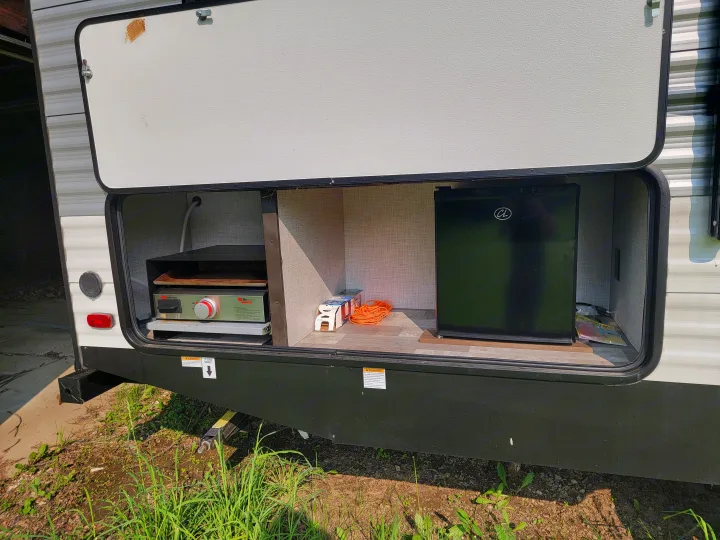 RV rental outdoor kitchen showing a griddle, mini-fridge, and storage. Ideal for convenient camping and outdoor cooking.. East to West Della Terra 2021