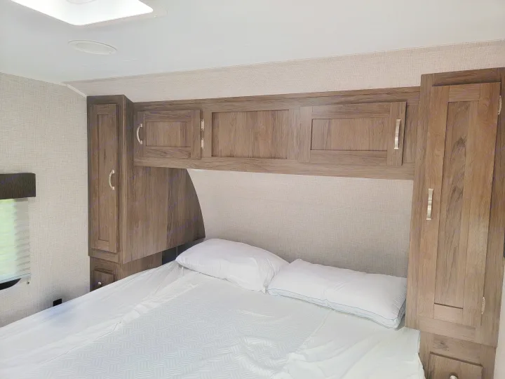 Cozy RV rental bedroom with a comfy bed, textured headboard, and ample wooden storage cabinets.. East to West Della Terra 2021