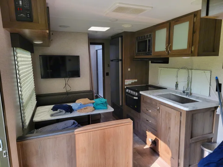 RV rental interior: kitchen with stove, sink, and cabinets, plus a dinette, TV, and bathroom entrance.. East to West Della Terra 2021