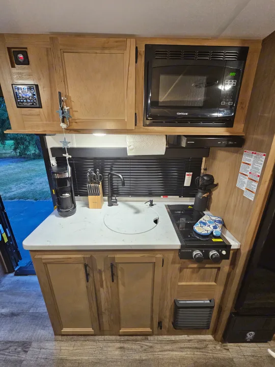 Functional RV rental kitchen space with a microwave, Greystone stove, sink, and ample wooden cabinetry.. Forest River Wolf pup 17JW 2023