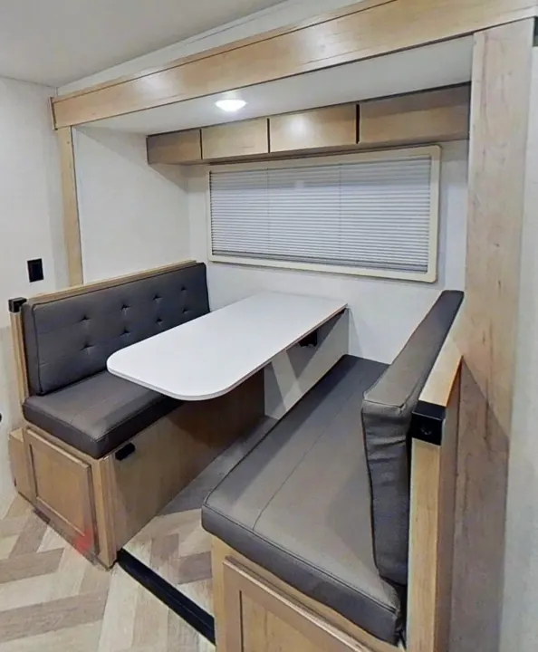 RV rental dinette featuring cozy gray benches, a light wood table, and overhead storage, perfect for meals on the road.. Ember 191MBD 2022
