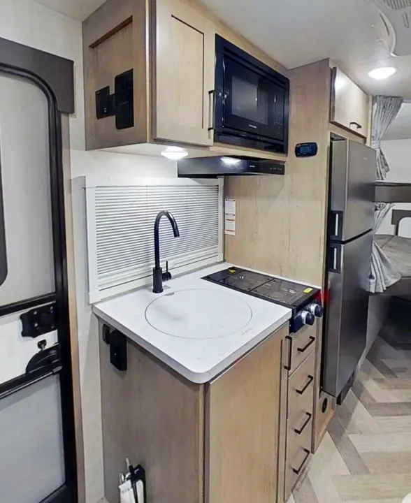 Experience compact living in this RV rental's kitchen, featuring a microwave, sink, stovetop, and stainless steel fridge.. Ember 191MBD 2022