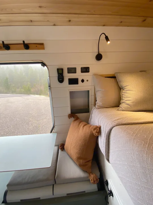Inside a modern **rv rental**, featuring a cozy bed, seating, controls, and a window looking out onto a misty, forested road.. Ford Transit custom 2019