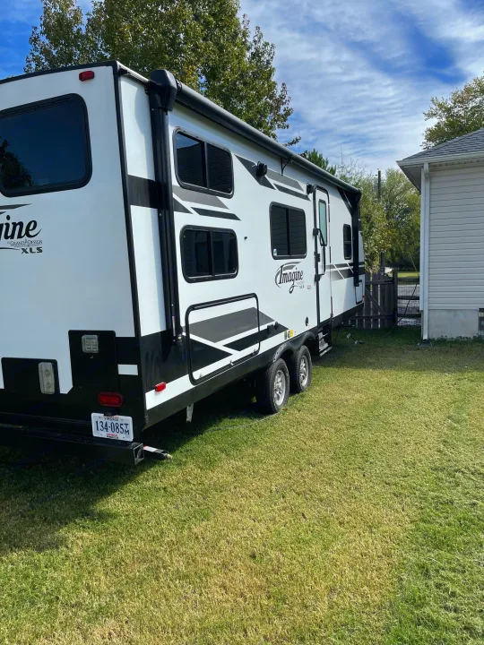 White Grand Design Imagine RV rental parked on green grass, ready for a trip. A house and trees are in the background.. Grand Design Imagine XLS 2022