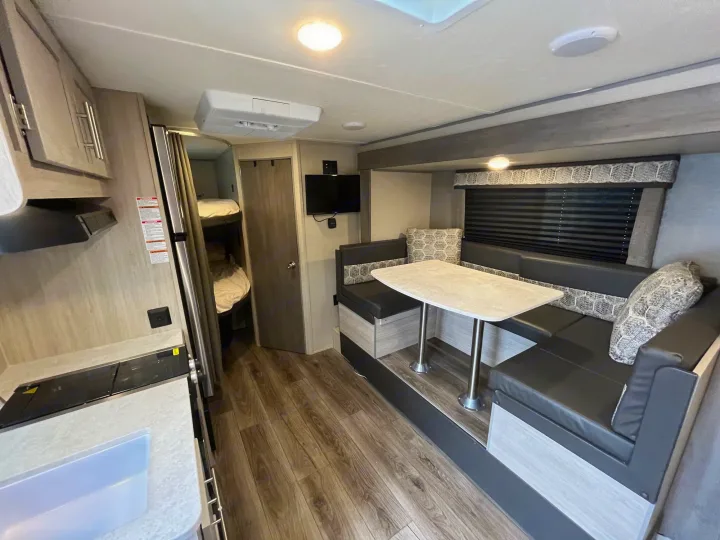 Modern RV rental interior with kitchen, dinette, mounted TV, and bunk beds. Wood-look flooring completes this functional space.. Coachmen Catalina Summit Series 7 2022