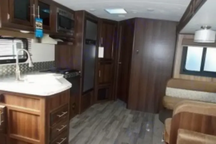 Inside a spacious RV rental: Modern kitchen with sink & stove, plus a cozy dining booth, all with dark wood cabinetry.. Jayco White Hawk 2018