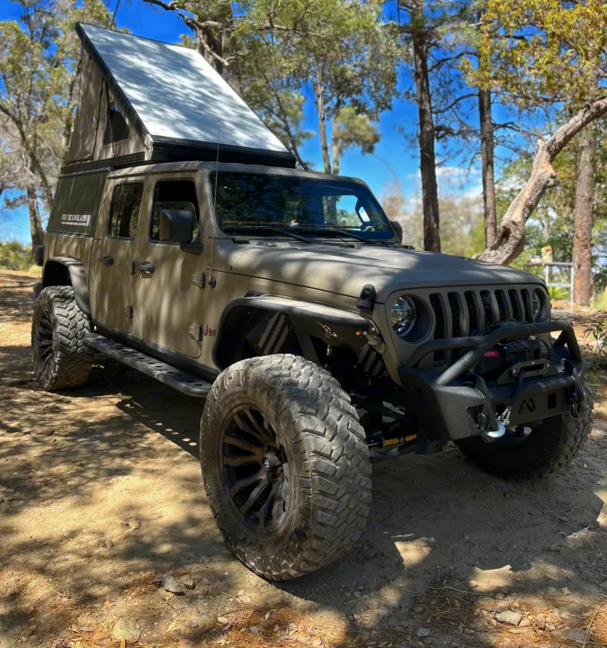 Custom Jeep Gladiator with a pop-top camper, large off-road tires, parked in a sunny forest. Perfect RV rental for adventures!. Jeep Gladiator Rubicon 2020