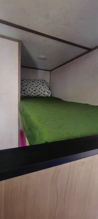 **RV rental** bunk bed interior: green comforter, patterned pillow with dinosaurs, light walls & ceiling. Compact sleeping space.. Dutchmen Coleman Lantern LT 2023