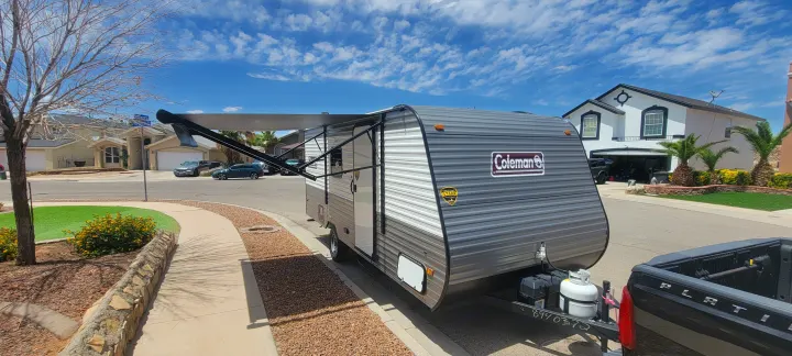 Coleman travel trailer with awning extended, hitched to a truck, on a sunny residential street. Ideal for an RV rental adventure.. Dutchmen Coleman Lantern LT 2023