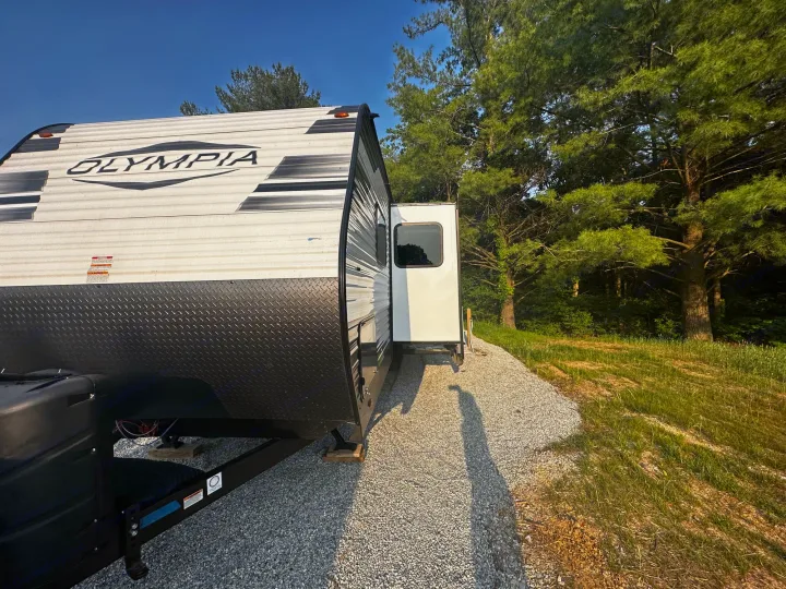 Enjoy nature with this Olympia travel trailer rv rental, parked on gravel beside green trees under a blue sky.. Highland Ridge RV Olympia 2022