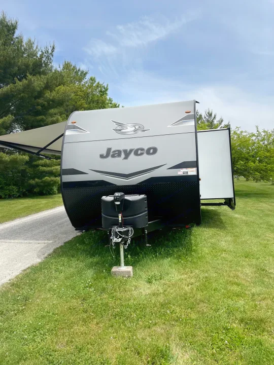Grey Jayco travel trailer RV rental parked on grass with awning out, perfect for outdoor living and adventure.. Jayco Jay Flight 2023
