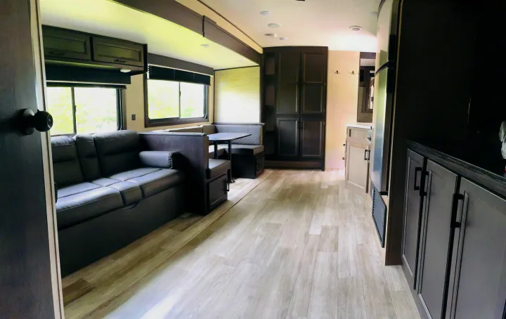 Experience comfort in this RV rental's inviting interior: dark sofa, U-shaped dinette, full kitchen, and light wood floors.. Jayco Jay Flight 2023