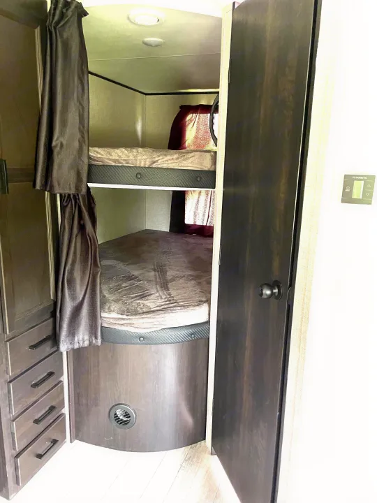 This RV rental features a compact sleeping area with two stacked bunk beds, privacy curtains, and a built-in storage cabinet.. Jayco Jay Flight 2023
