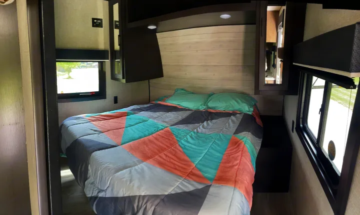Comfortable RV rental bedroom with a bed, teal & pink geometric comforter, overhead storage, and windows. Ideal for travel.. Jayco Jay Flight 2023