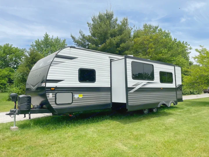 A modern Jayco travel trailer RV rental, featuring an extended slide-out, parked on green grass under a blue sky.. Jayco Jay Flight 2023