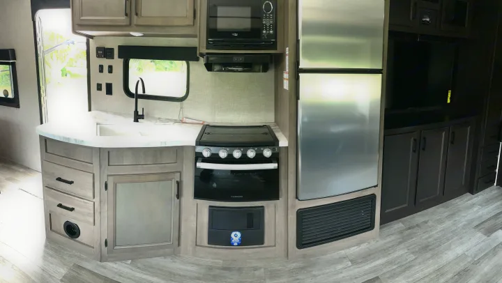 Modern RV rental kitchen with stainless steel appliances, sink, oven, fridge, and entertainment setup.. Jayco Jay Flight 2023