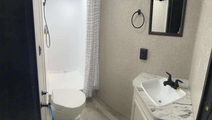 Functional RV rental bathroom with white toilet, stand-up shower with plaid curtain, and black-fauceted sink.. Jayco Jay Flight 2023