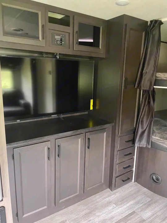 Spacious RV rental interior featuring a TV, dark wood-look cabinetry with storage, and private bunk beds, ideal for travel.. Jayco Jay Flight 2023