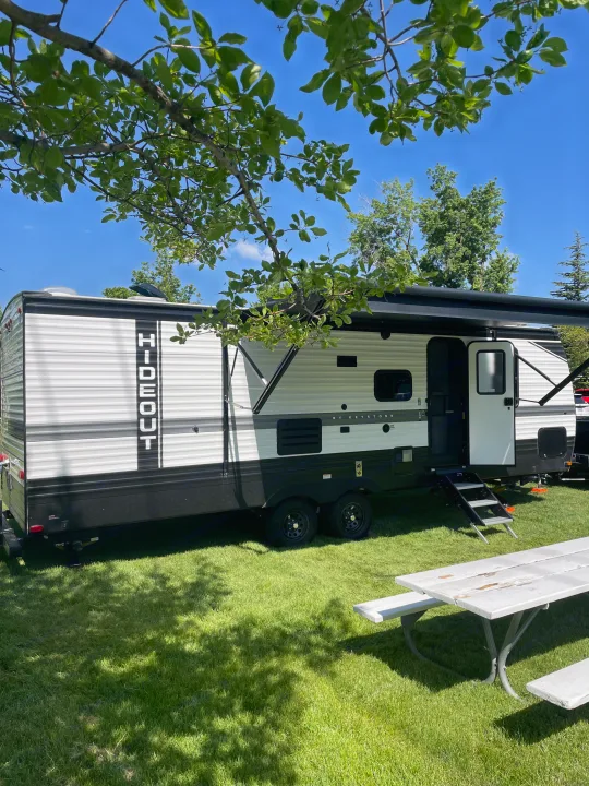 A white and black Hideout by Keystone travel trailer (rv rental) parked on green grass with an open awning and picnic table. Sunny day.. Keystone RV Hideout 2022