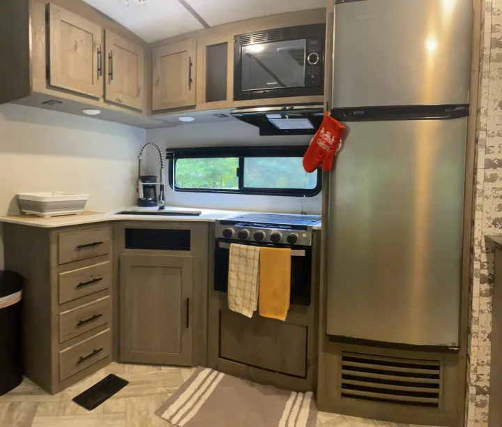 Modern RV rental kitchen with stainless steel fridge, microwave, stove, and sink. Ample light cabinets and counter space for comfort.. Keystone RV Springdale 2021