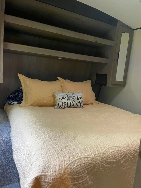 Cozy RV rental bedroom featuring a comfy bed with quilted bedding, a welcome pillow, and built-in storage.. Keystone RV Springdale 2021