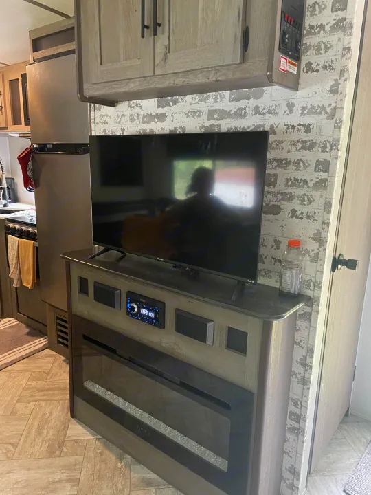 Modern RV rental interior with a living space featuring a TV, electric fireplace, kitchen, and refrigerator.. Keystone RV Springdale 2021