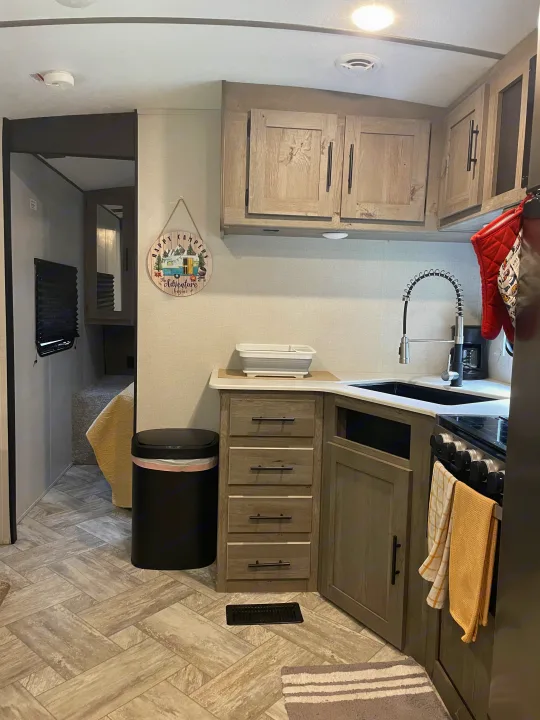 Cozy RV rental interior with a functional kitchen, including wood-look cabinets, sink, and a stove, plus a bunk area.. Keystone RV Springdale 2021