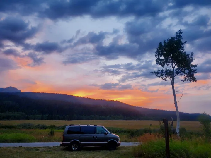 Charcoal van at serene sunset, mountains & forest backdrop. Ideal RV rental escape.. Chevrolet Open Road 2000