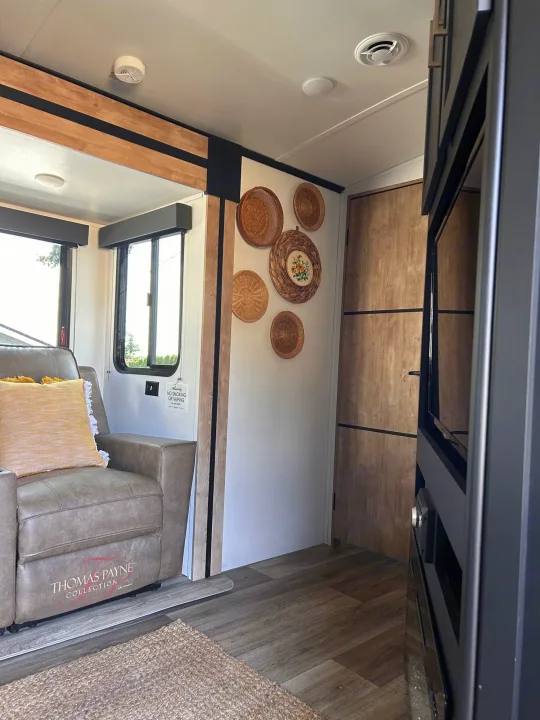 Relax in this cozy RV rental's living area! Features a plush recliner, bright windows, TV, and charming decor.. Keystone RV Outback Ultra-Lite 2022
