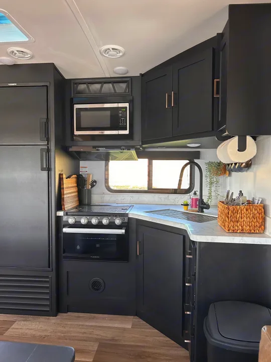 Clean, modern black kitchen in an RV rental, with full-size fridge, microwave, stove, and light countertops.. Keystone RV Outback Ultra-Lite 2022