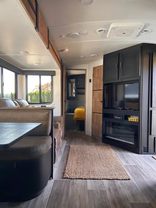 Modern RV rental interior: living space with dining booth, entertainment unit, and a cozy bedroom beyond.. Keystone RV Outback Ultra-Lite 2022